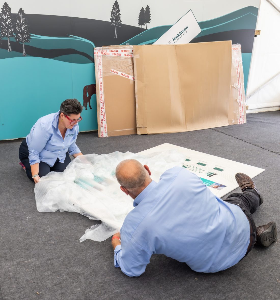 Two people unwrap the signage made for the exhibition