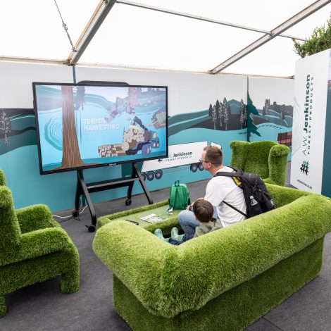 A man and child sit on the green sofas, watching an AW Jenkinson video on a TV