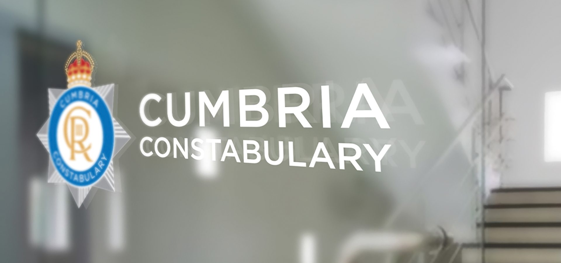 Cumbria Constabulary's new and updated police crest, featuring King Charles lll's cypher on a glass door as a window vinyl in an official building.