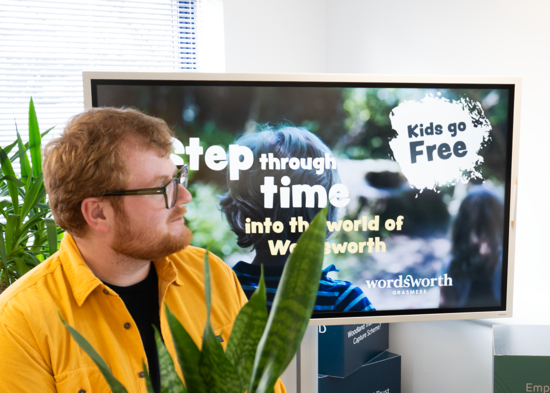Image of Callum sitting in front of a large screen showcasing the Wordsworth grasser digital marketing social media camapign