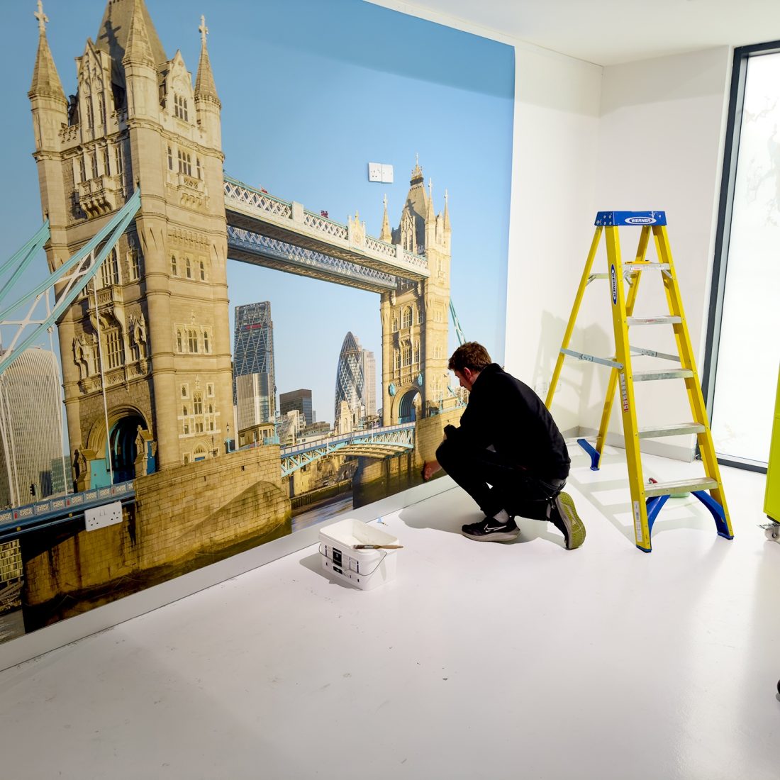 Marco installing a Digimura digital wallcovering of a photo of London Bridge at the Papergraphics headquarters.