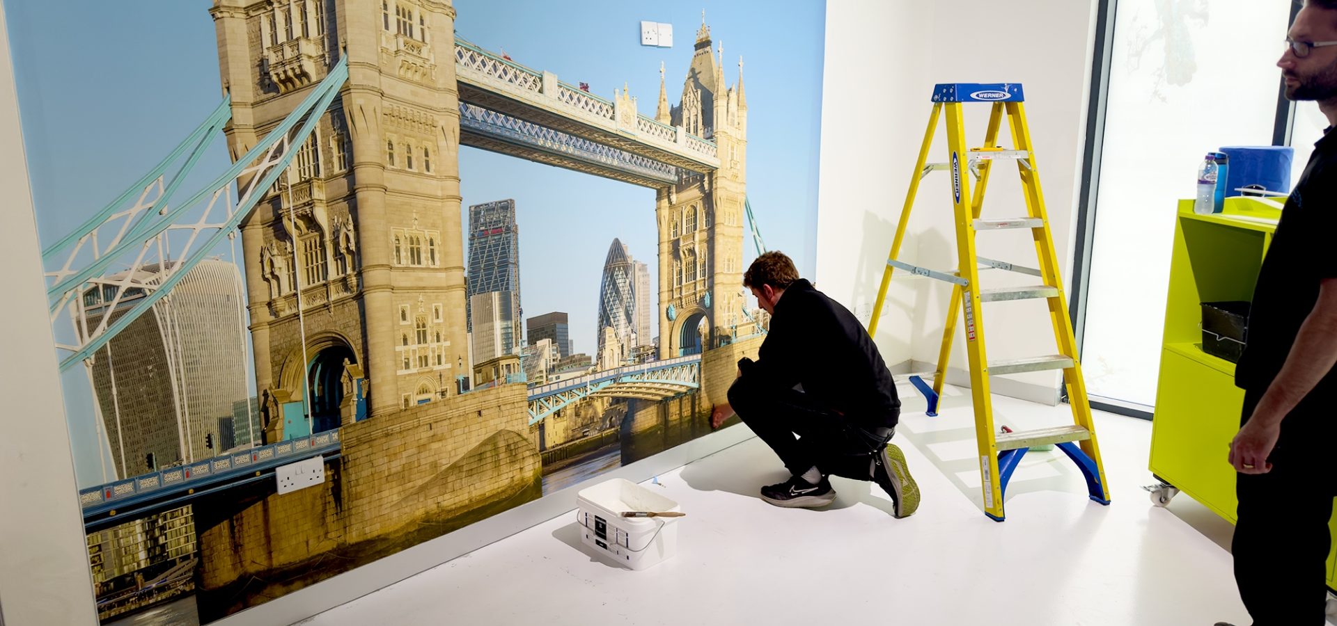 Marco installing a Digimura digital wallcovering of a photo of London Bridge at the Papergraphics headquarters.